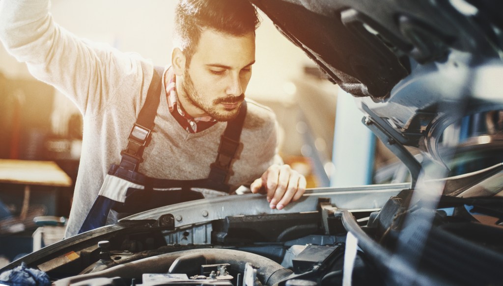 Closeup of mechanic in engine bay, preparing a car for the summer season.